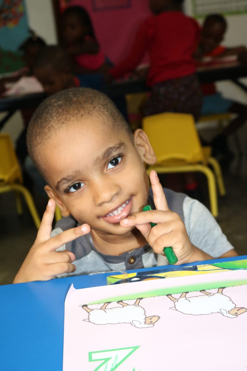 A preschool boy smiling at his desk during class