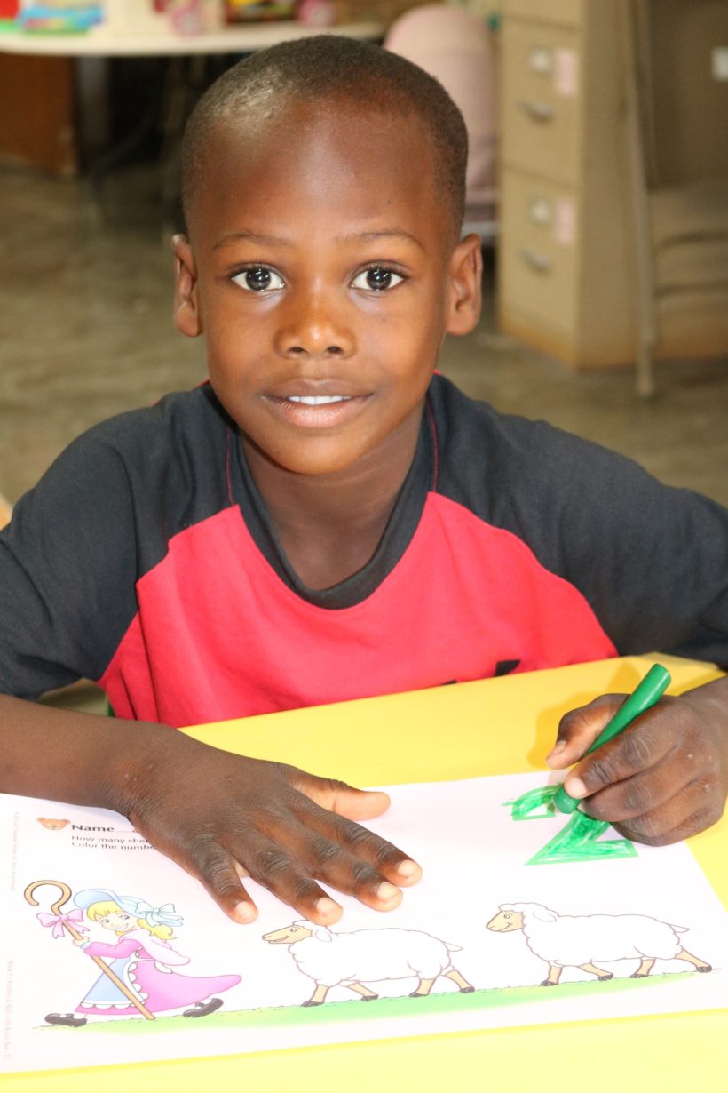 A preschool boy colouring a worksheet with a green crayon
