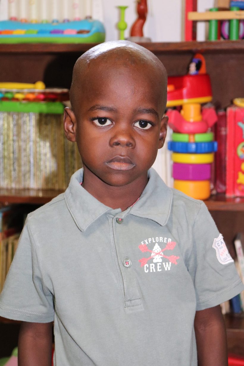 A preschool boy in a grey polo shirt in the classroom